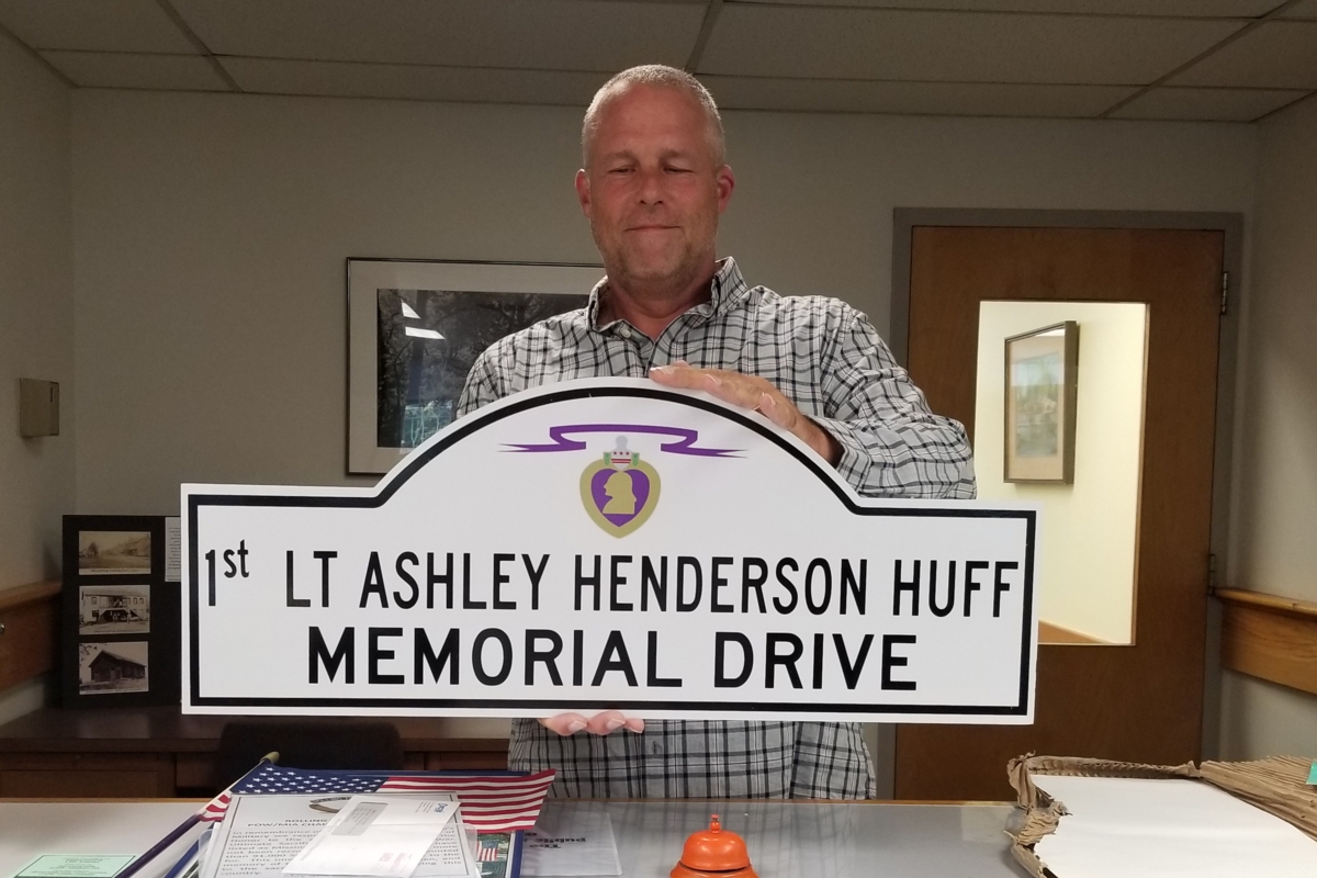 Mike Maloney, Chairman of the Montgomery Veterans Memorial Committee, proudly holds the new street sign honoring Ashley. The sign, displaying the Purple Heart insignia, was designed by a member of the veterans advocacy grgroup “Rolling Thunder”.